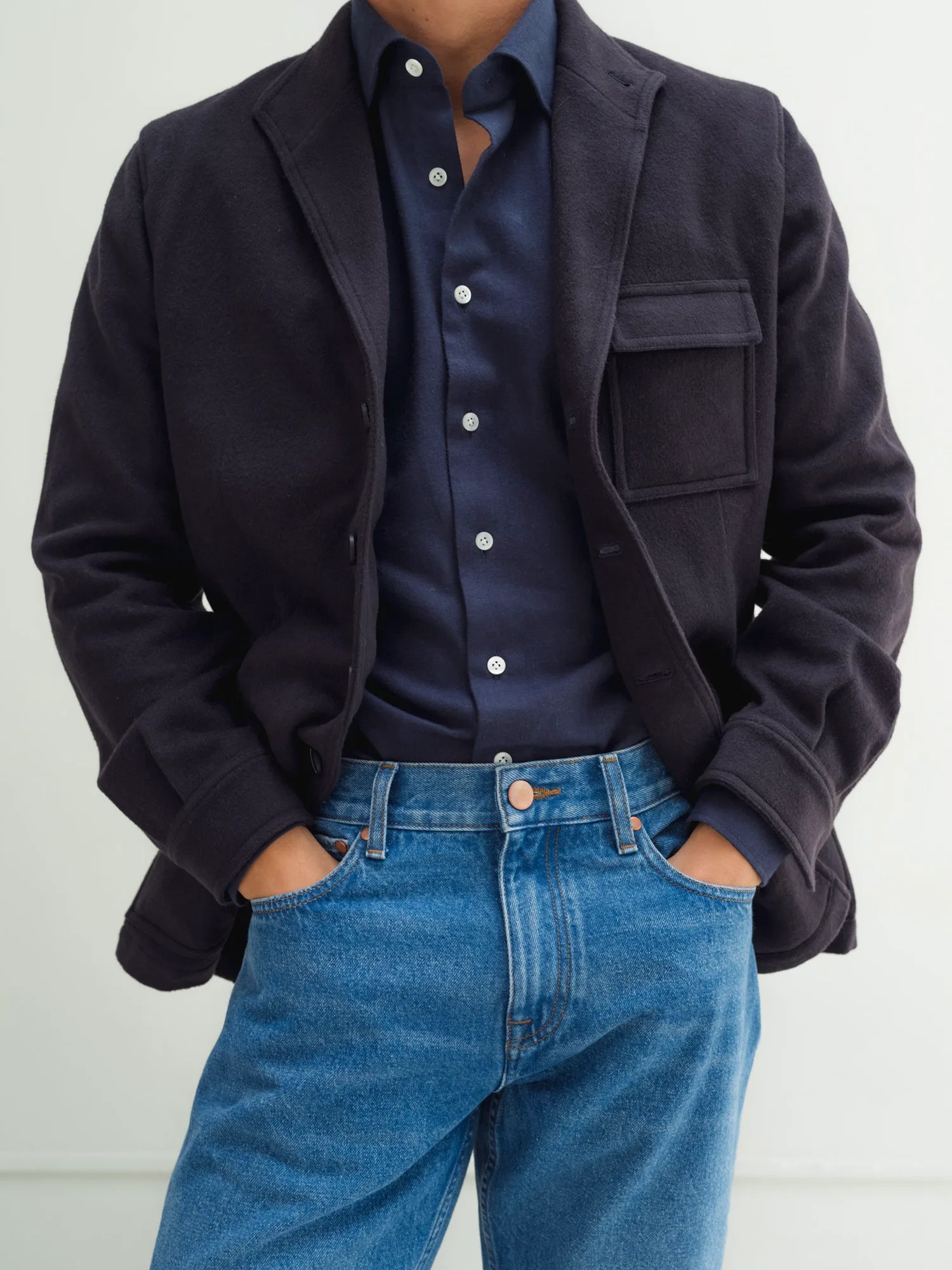 Dark jacket and dark blue shirt over light jeans, cropped at the hip