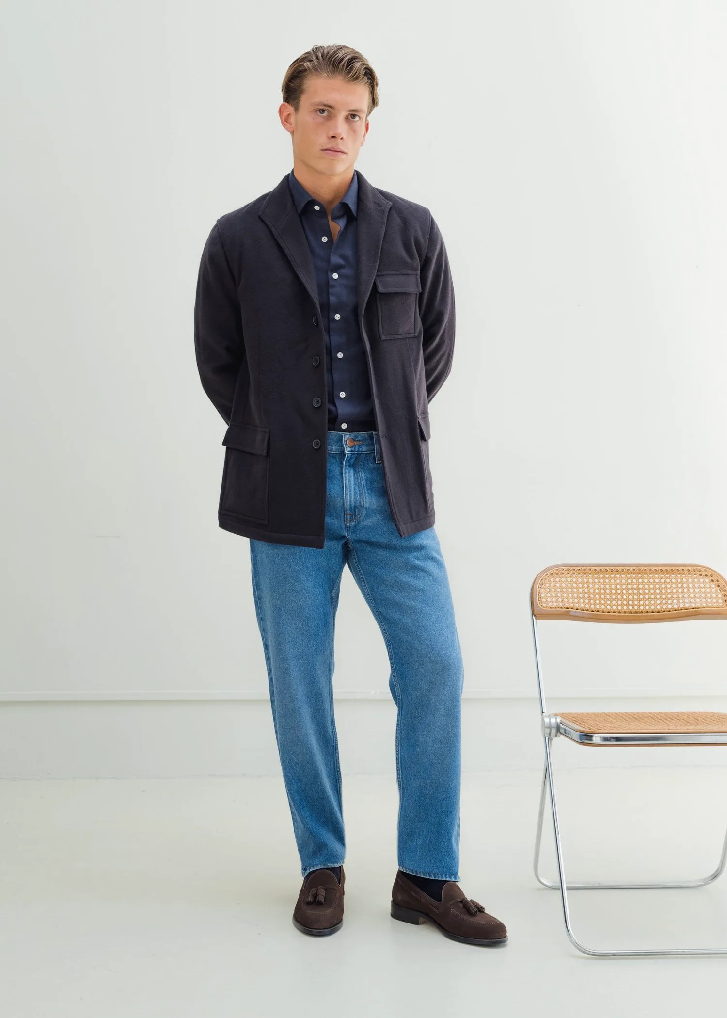 Man in a dark overshirt and jeans by a folding chair