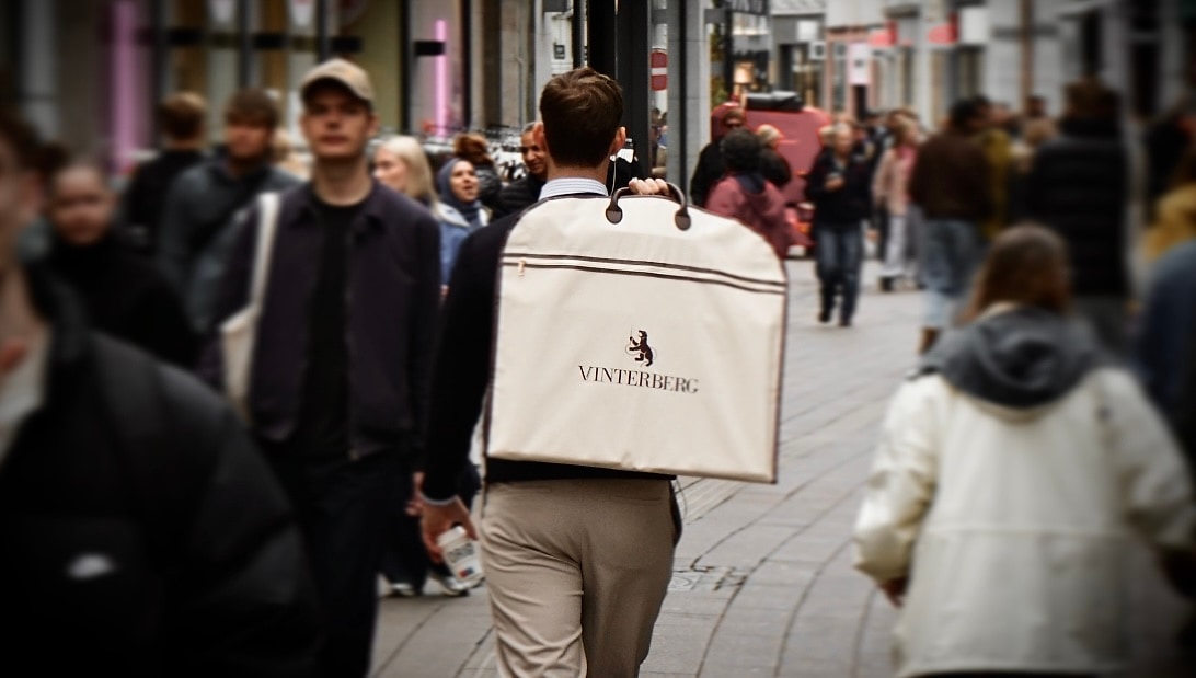 Man walking through a pedestrian street with a Vinterberg garment bag over his shoulder