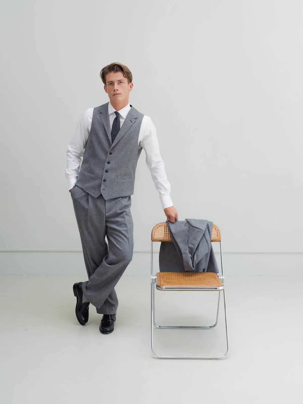 Man in a grey striped waistcoat and trousers with the jacket on a folding chair