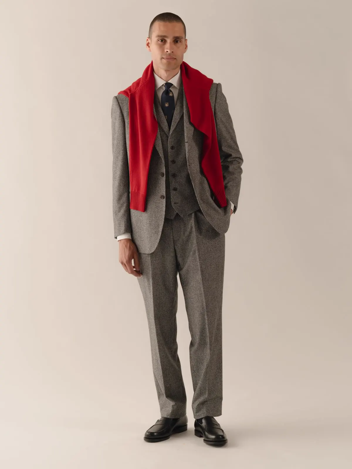 Man in a grey checked three-piece suit with a red scarf over his shoulders