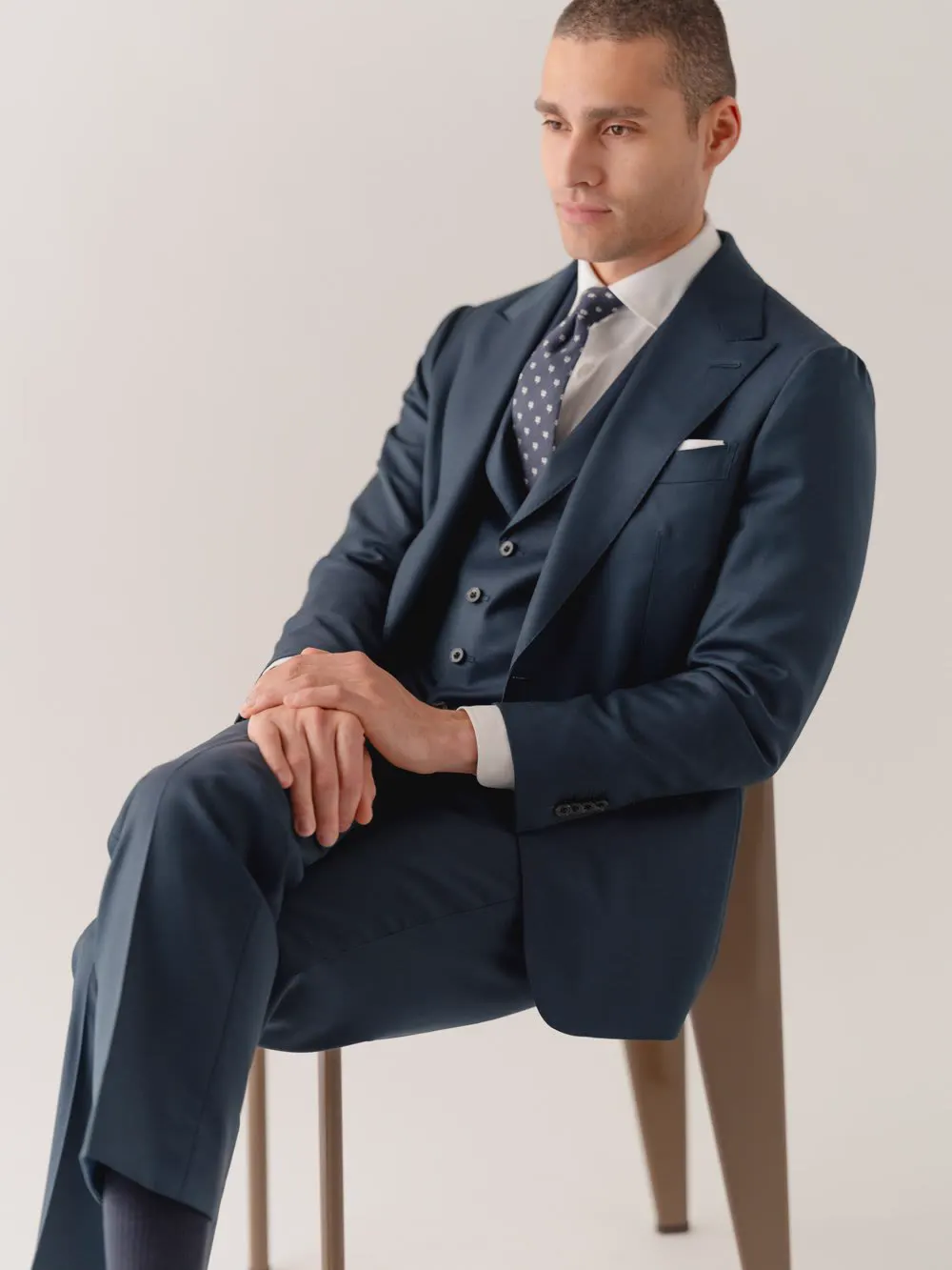 Man in a navy three-piece suit seated on a chair