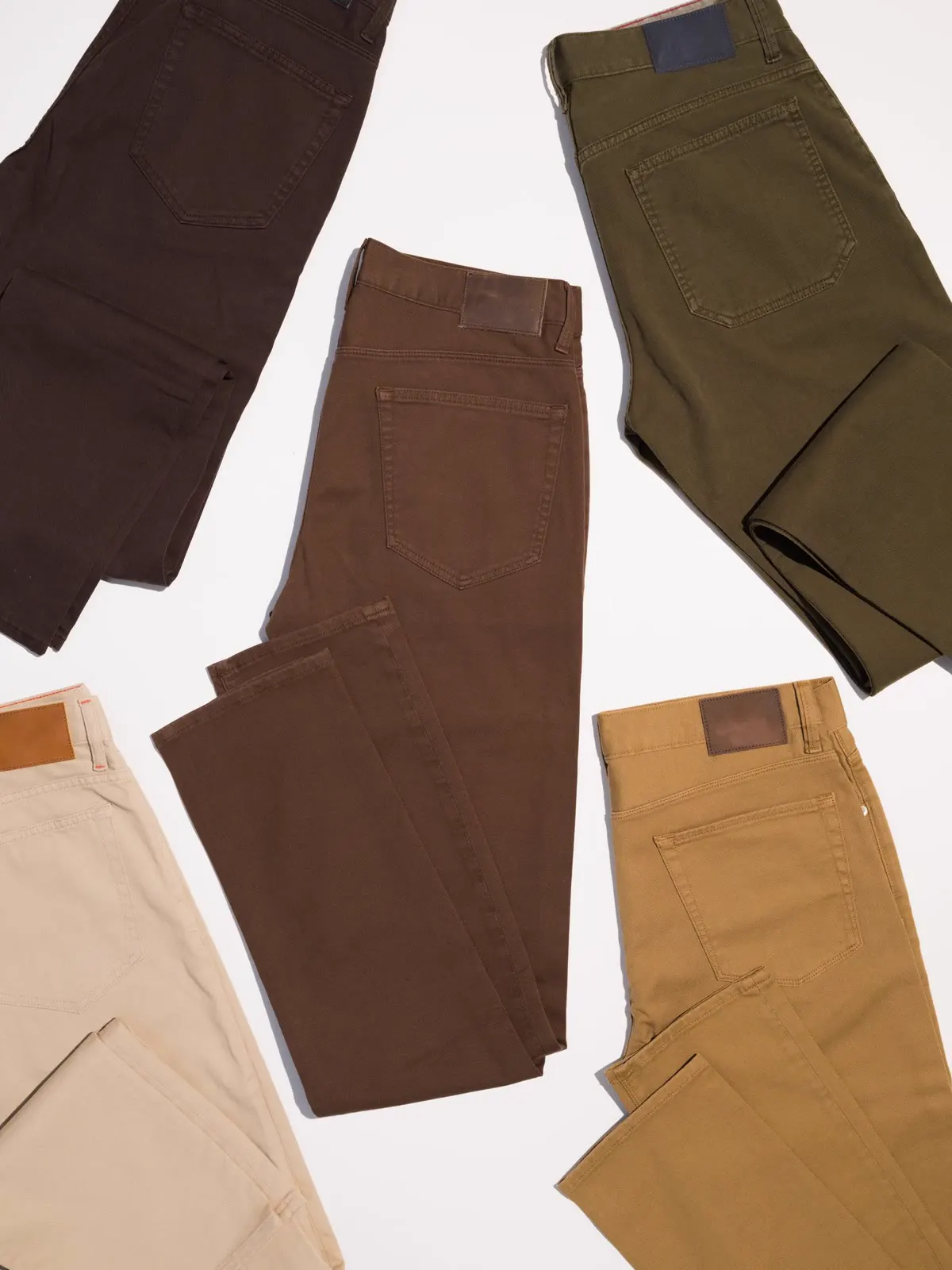 Chinos i brun, oliven, sand og okker lagt på hvid baggrund