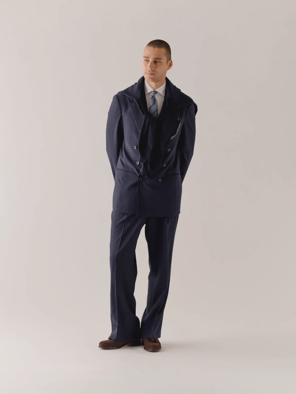 Man in a navy double-breasted suit with his hands behind his back