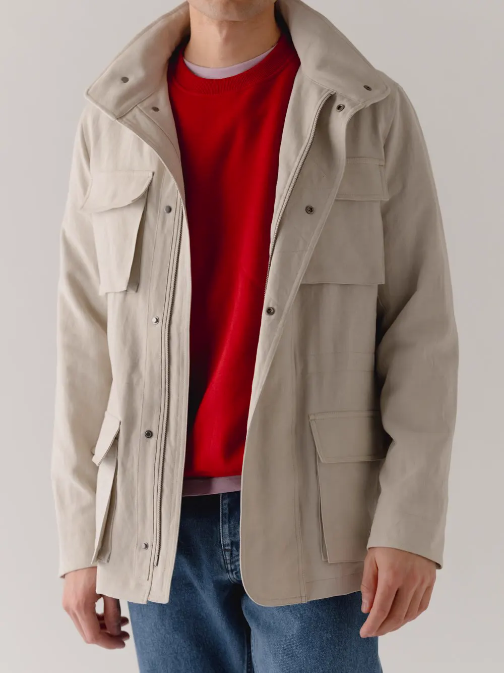Lys field jacket med fire klaplommer over rød strik og jeans