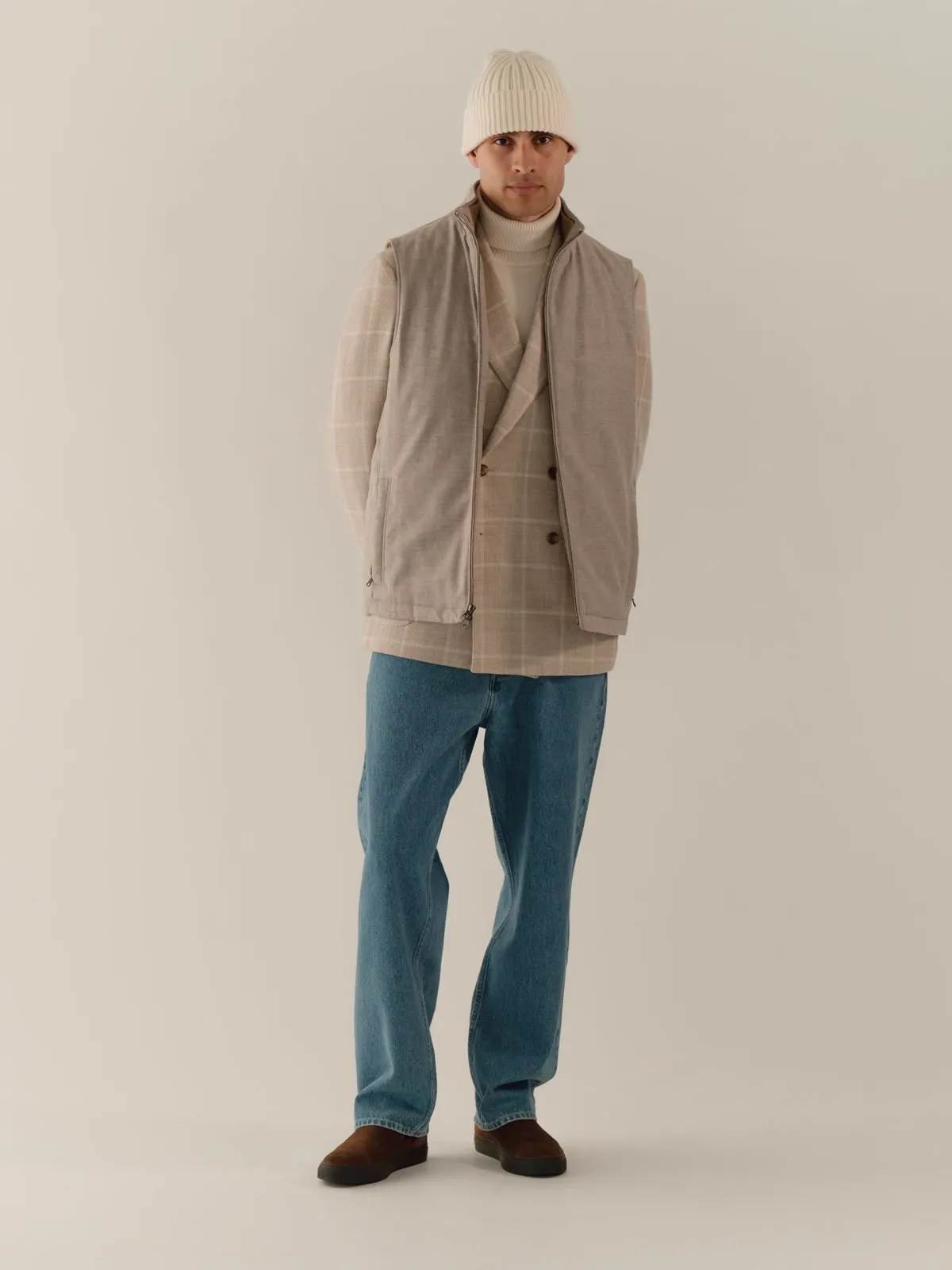 Mand i lys quiltet gilet over ternet skjorte, jeans og hue