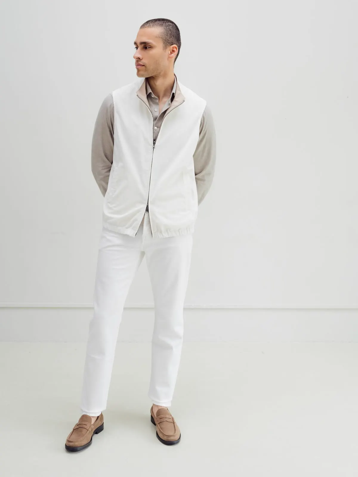 Man in a light gilet over a grey shirt and white trousers