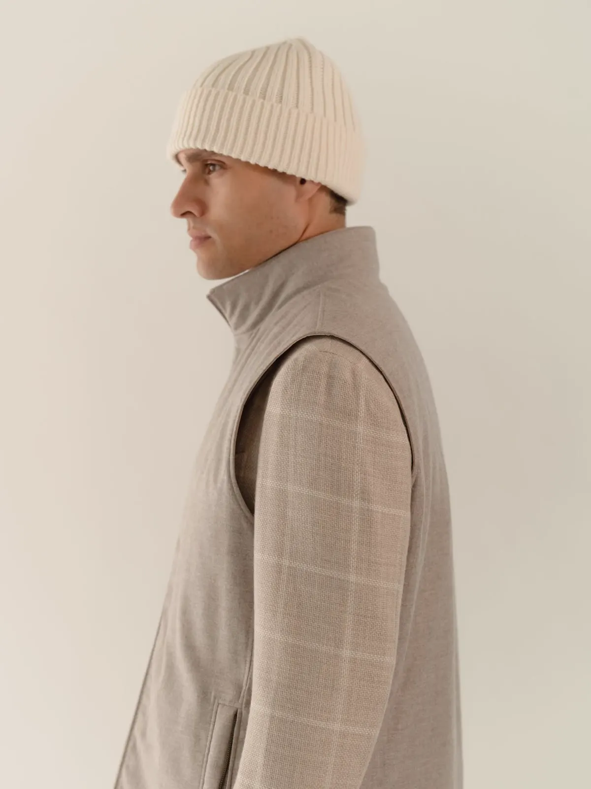Man in a grey gilet over a checked shirt and beanie, seen from the side