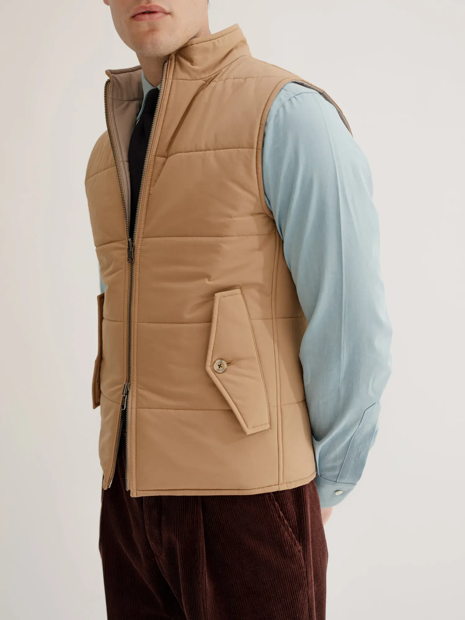 Man in a camel quilted gilet over a light blue shirt and dark tie
