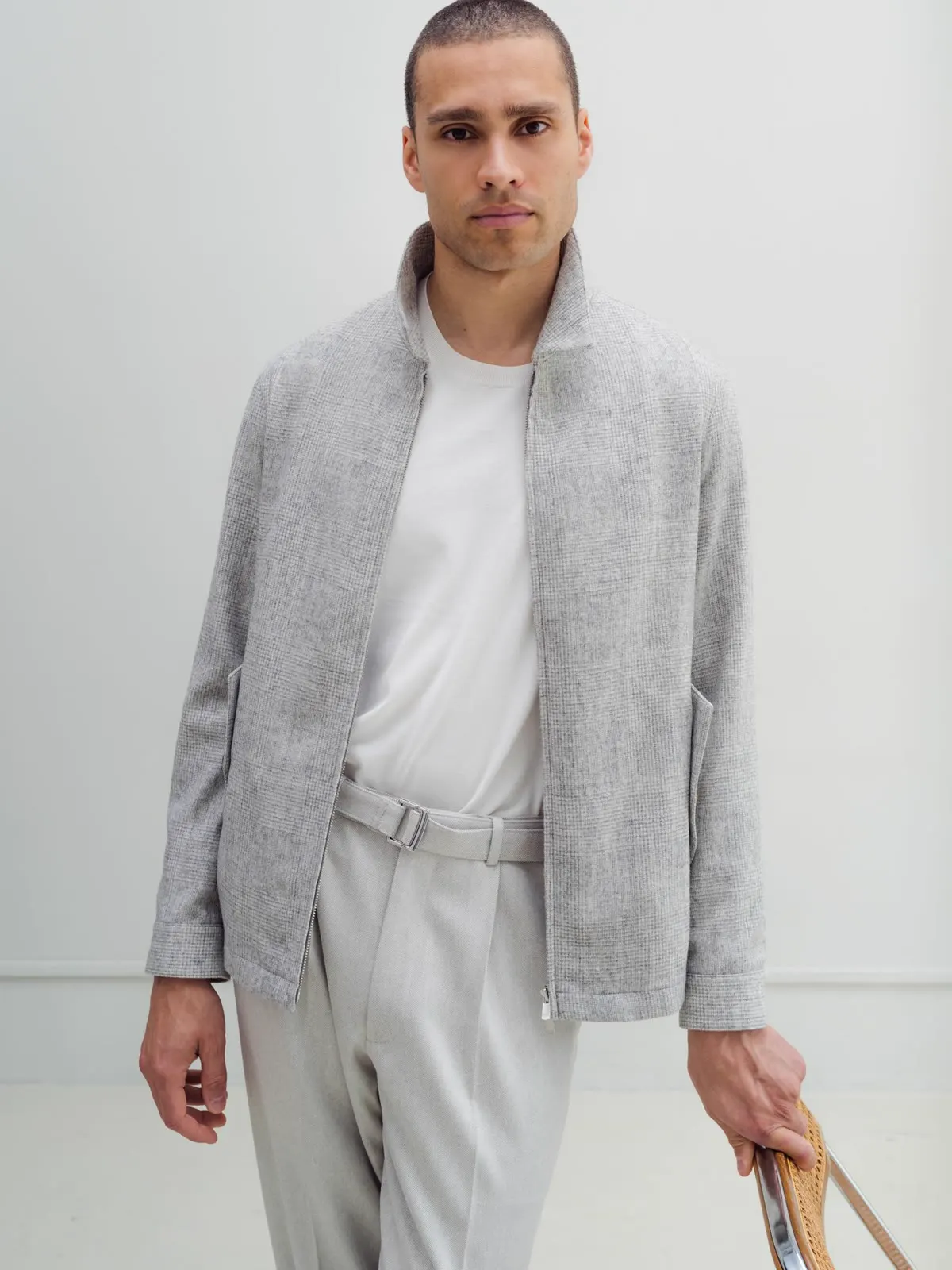 Man in a light grey short jacket with a zip over a white T-shirt and light trousers