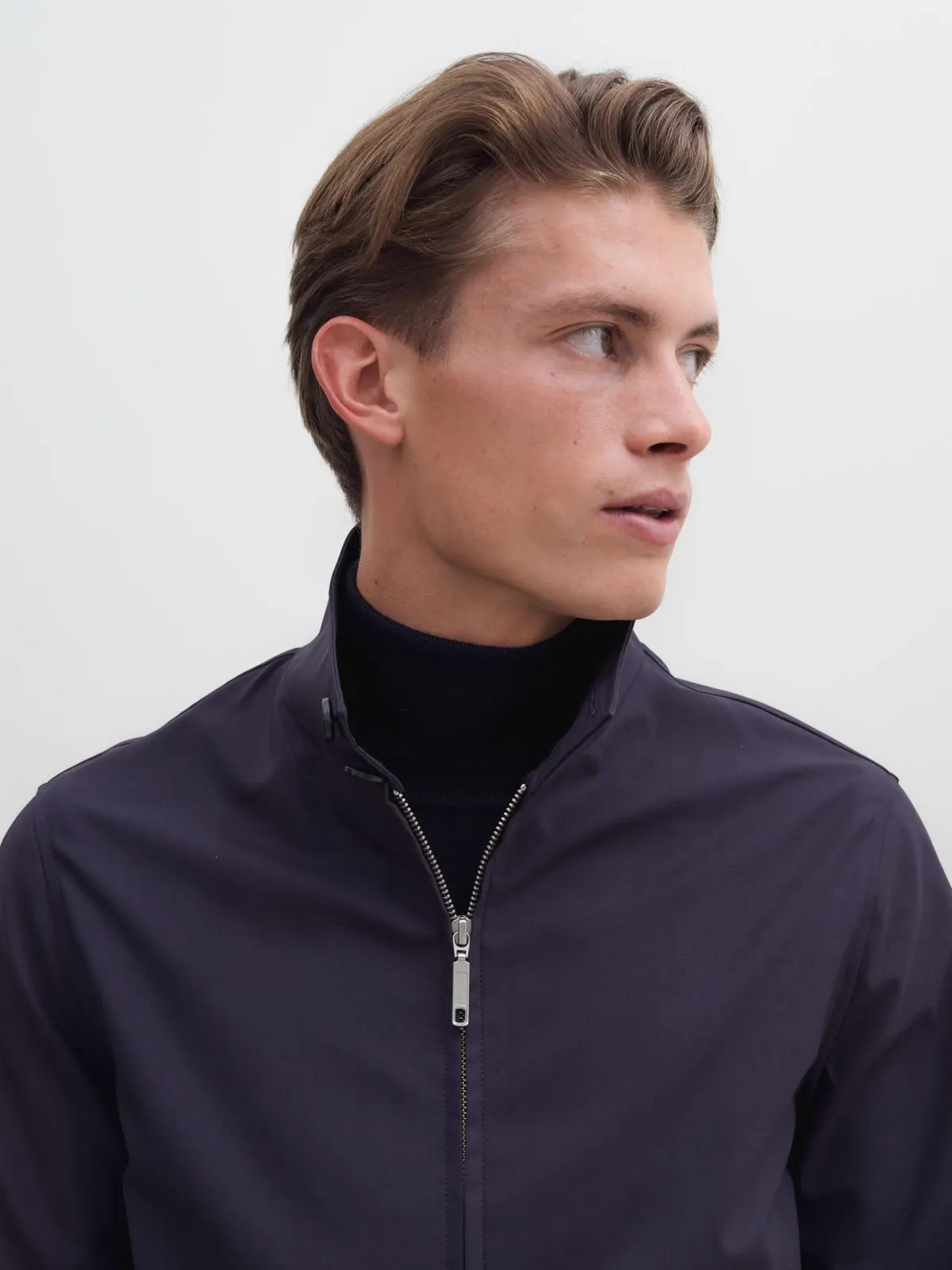 Man in a dark short jacket with a zip over a black roll neck
