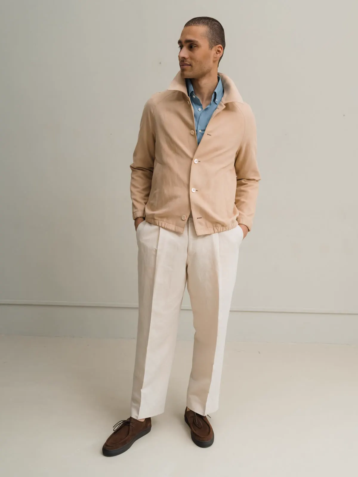 Man in a light short jacket over a light blue shirt and white trousers
