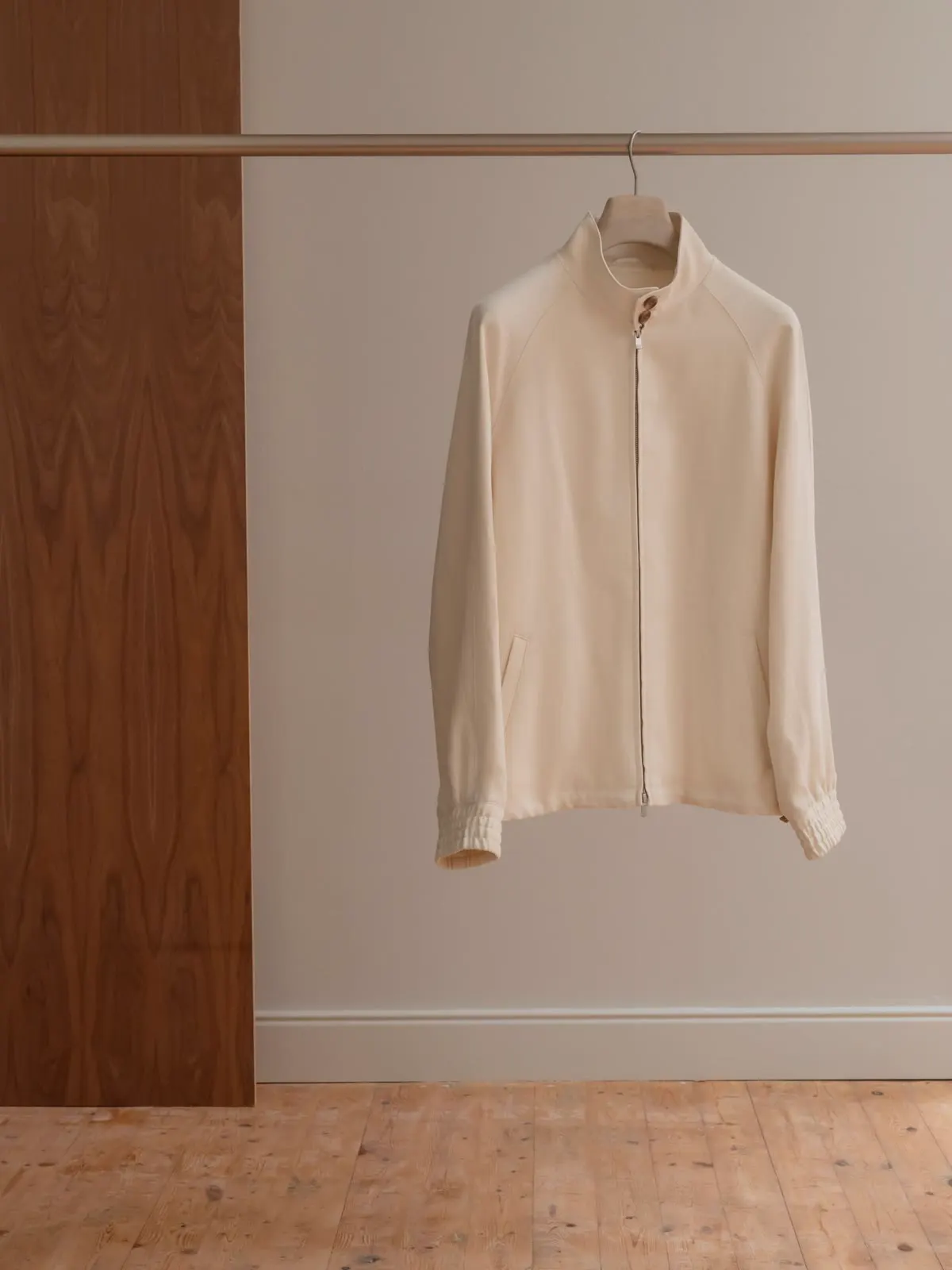 Light Harrington jacket hung on a rail in front of a light wall
