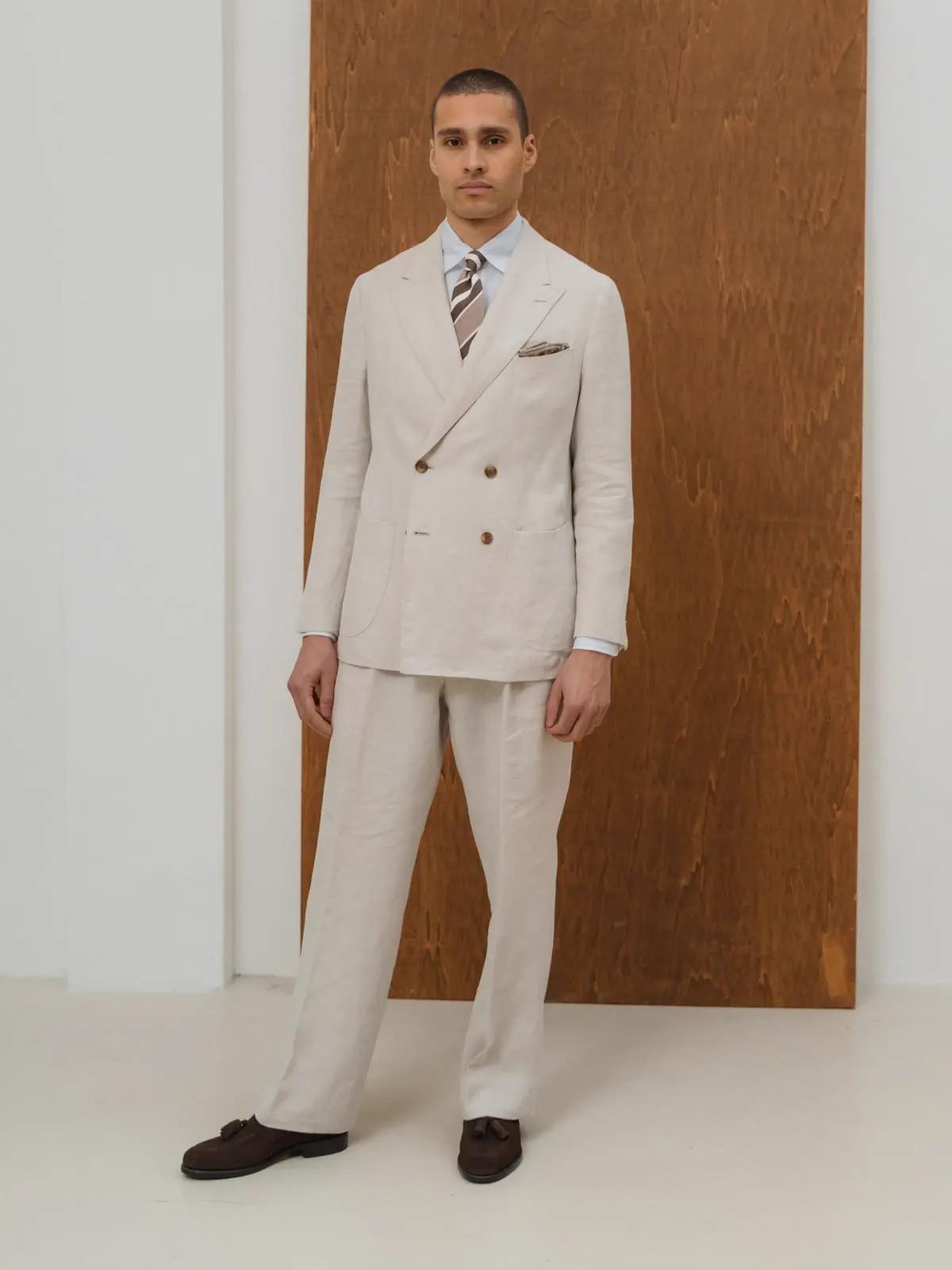 Man in an off-white double-breasted suit in front of wood panelling