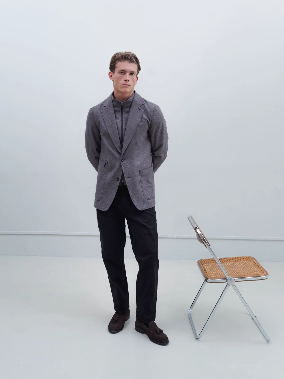 Man in a grey hybrid jacket and dark trousers by a folding chair