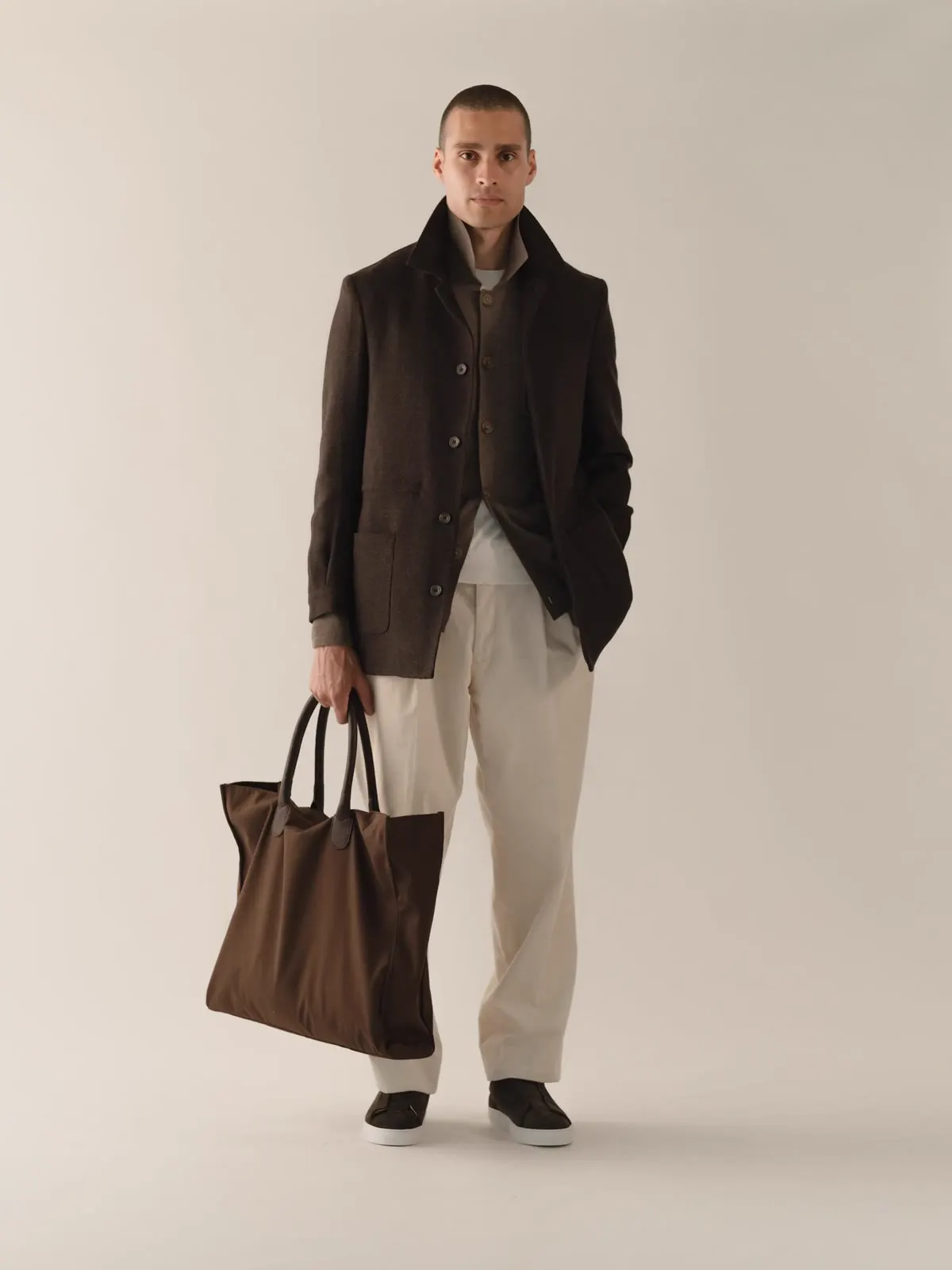Man in a dark brown hybrid jacket and light trousers, with a brown bag