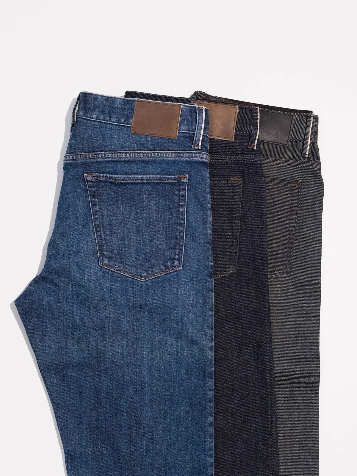 Three pairs of jeans in blue, black and grey hung over one another