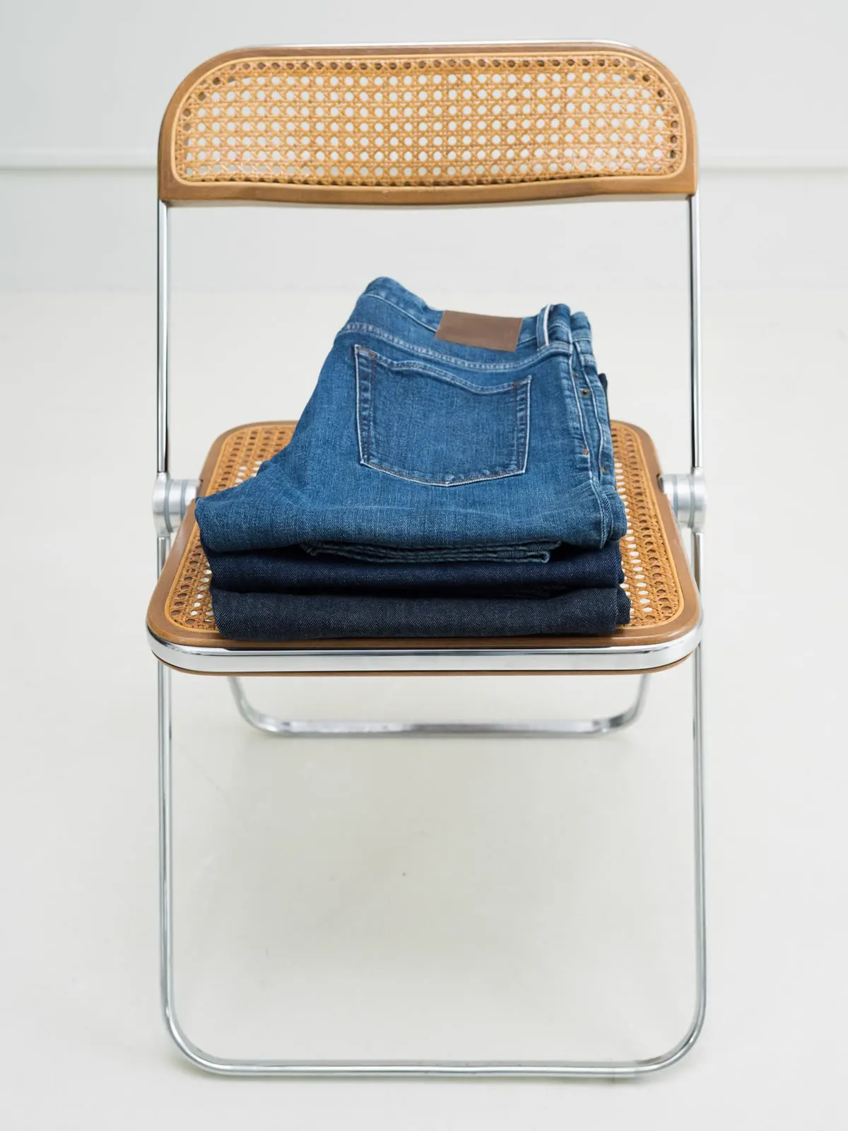 Stack of folded jeans on a folding chair with a woven seat