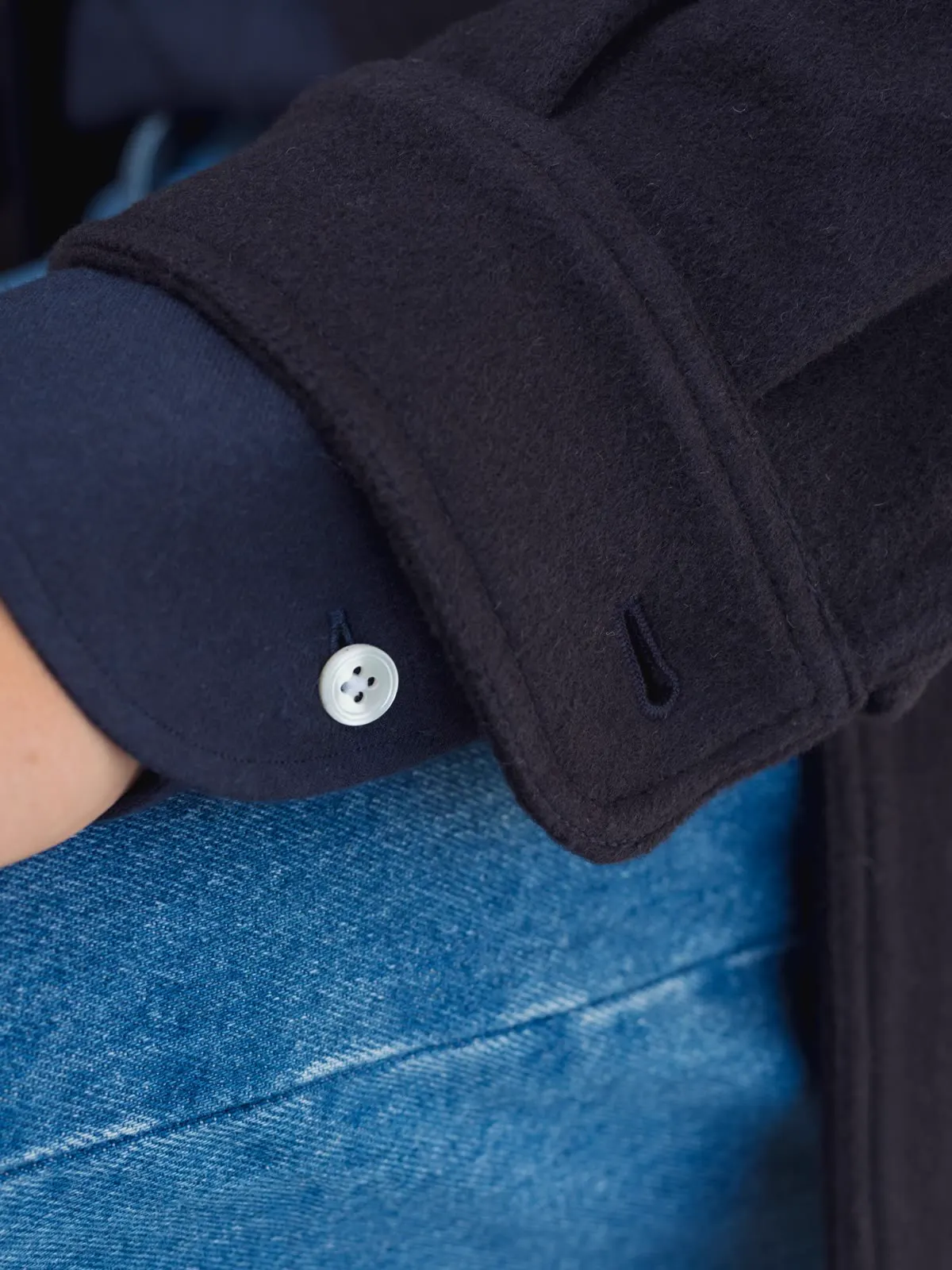 Close-up of a dark blue overshirt with a button on the cuff, over jeans
