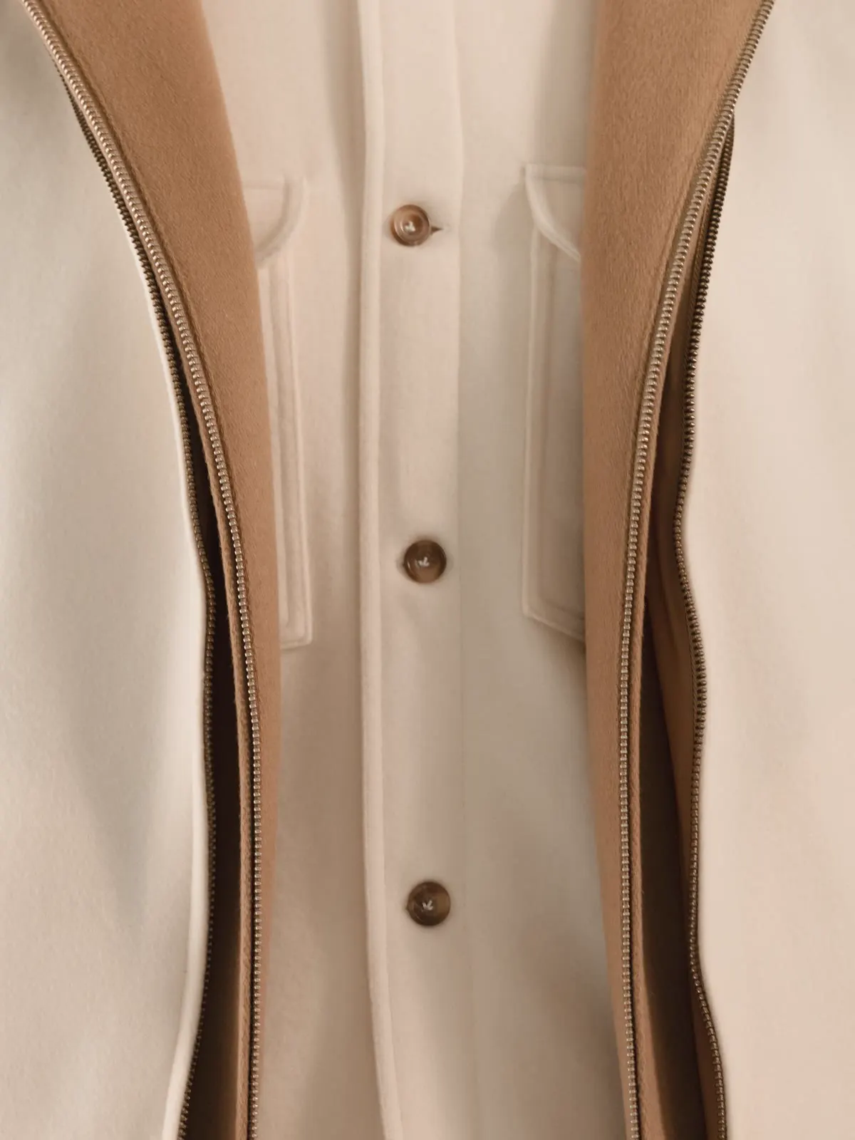 Close-up of the buttons on a light overshirt between the edges of a brown gilet