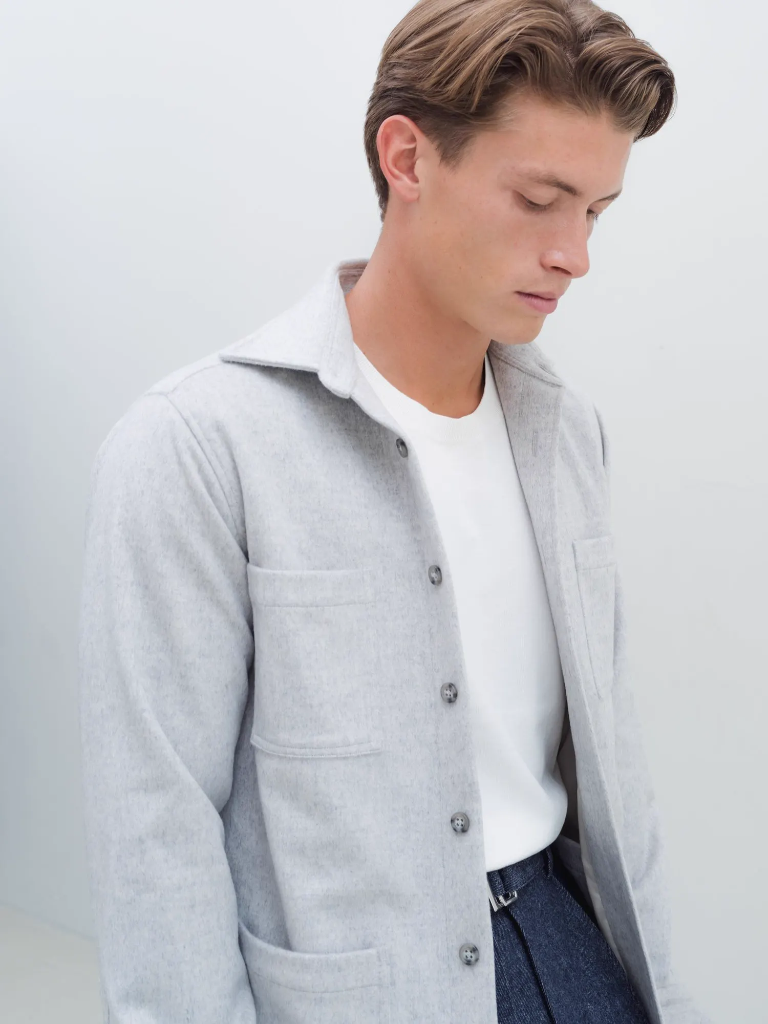 Man in a light grey overshirt with chest pockets over a white T-shirt, seen from a three-quarter angle