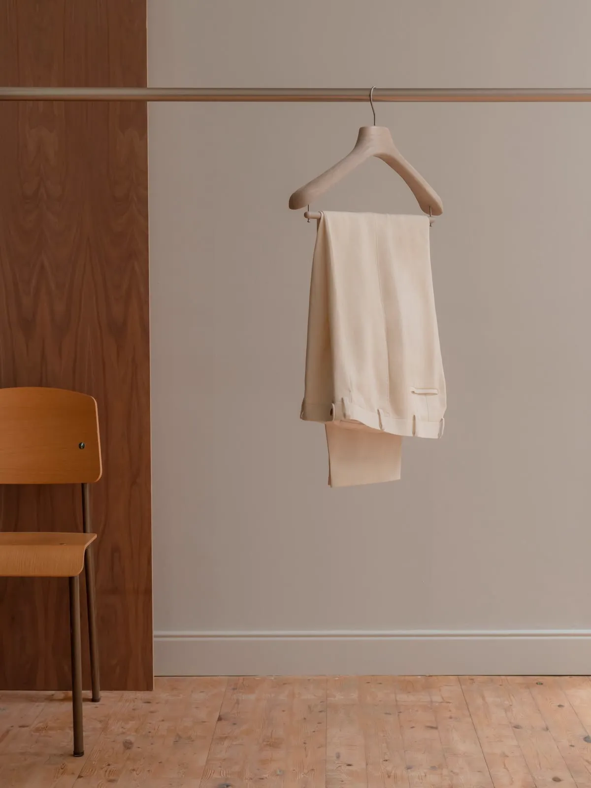 Light trousers folded over a hanger in front of wood panelling