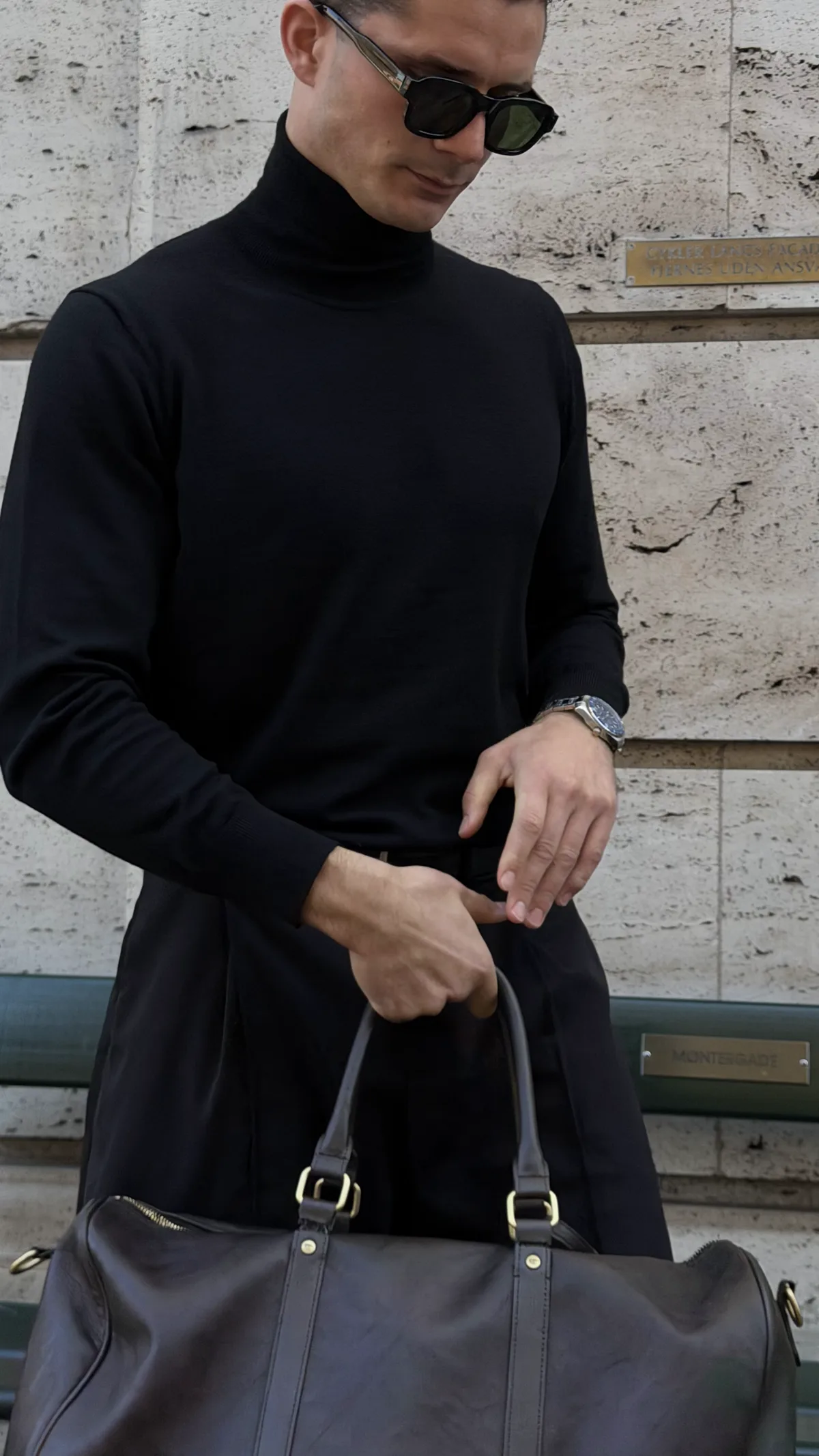 Sort merino-rullekrave i profil foran rå facade