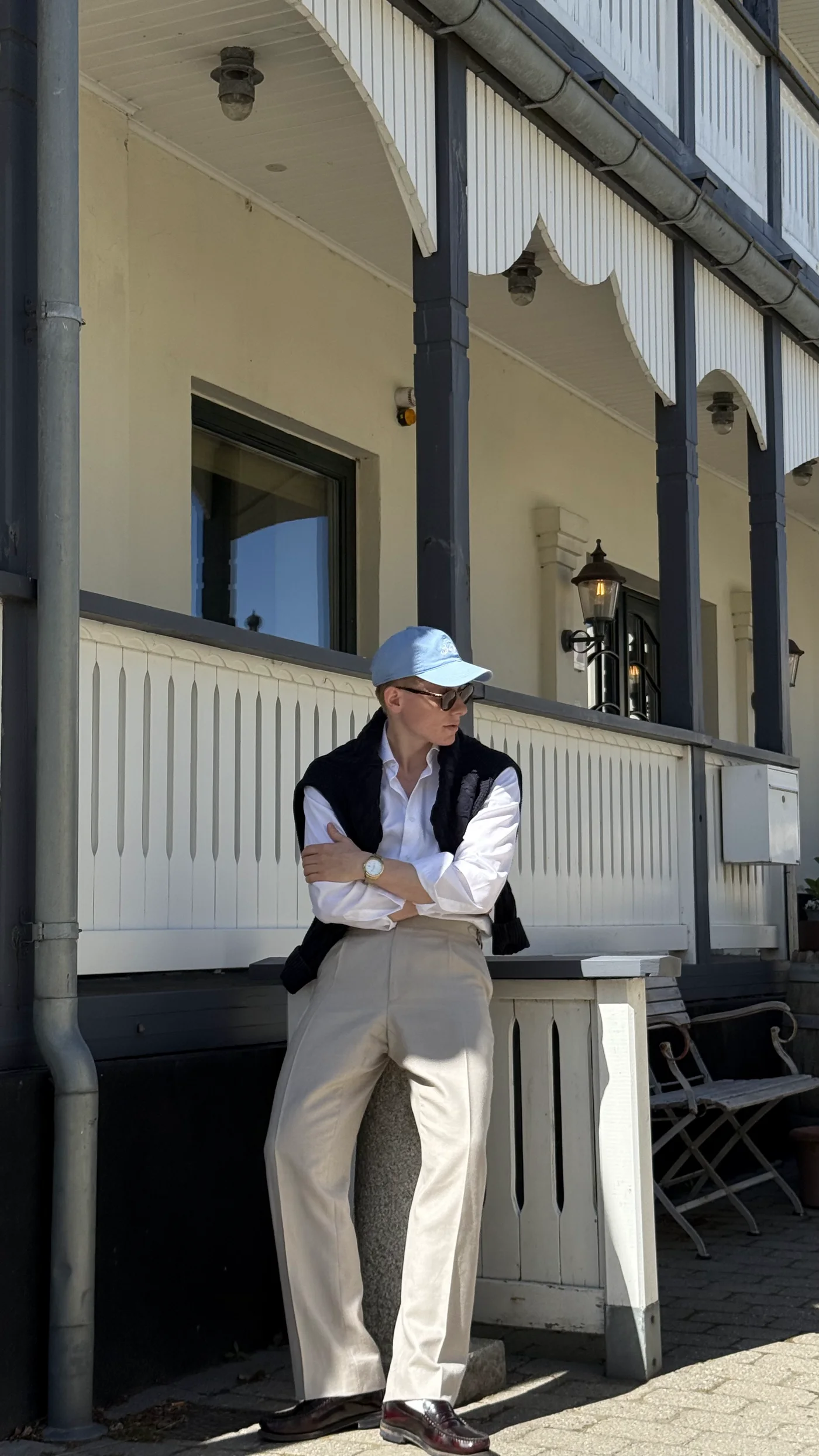 Hvid skjorte med navy vest og kasket på veranda