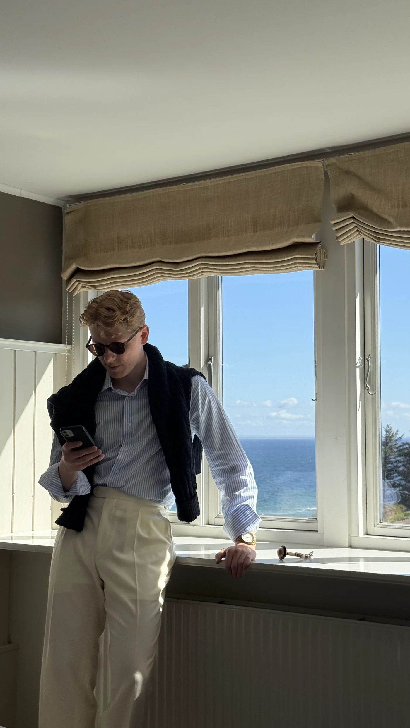 Hvid skjorte med navy vest ved vindue med havudsigt