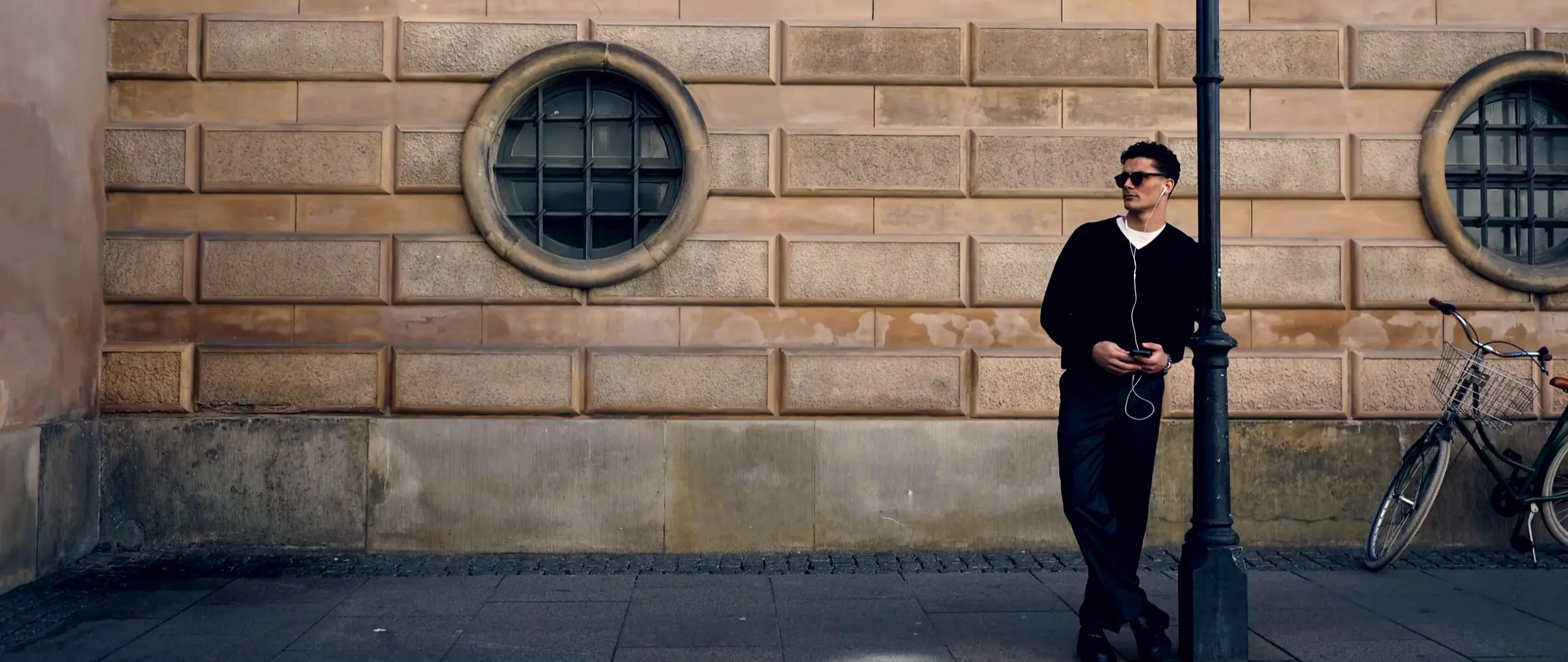 Man in black knitwear by the sandstone facade with the round windows in Copenhagen