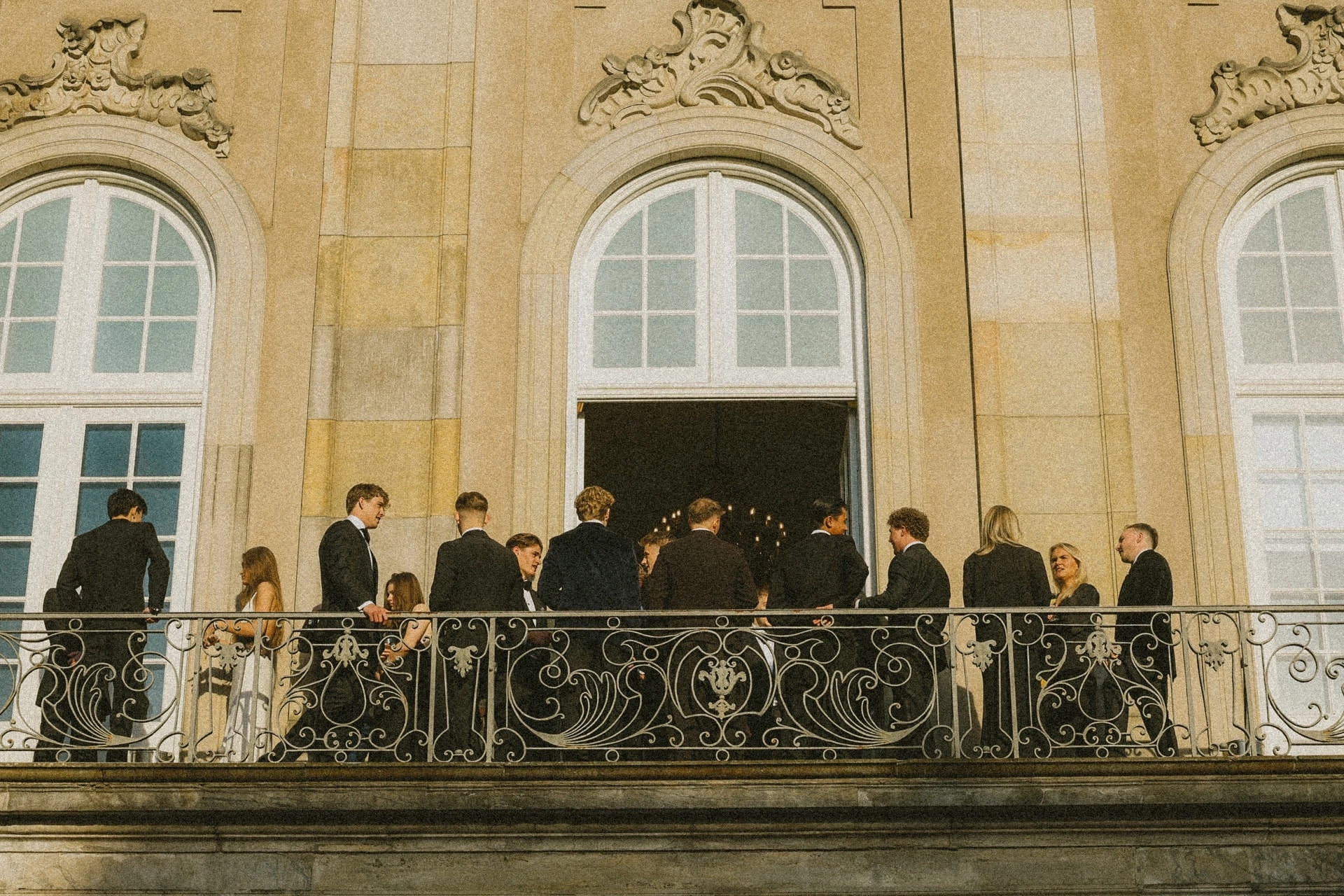 Guests in dark suits and black tie on a balcony at a festive occasion
