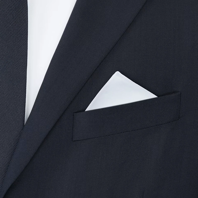 White pocket square with one point up in the breast pocket of a navy jacket