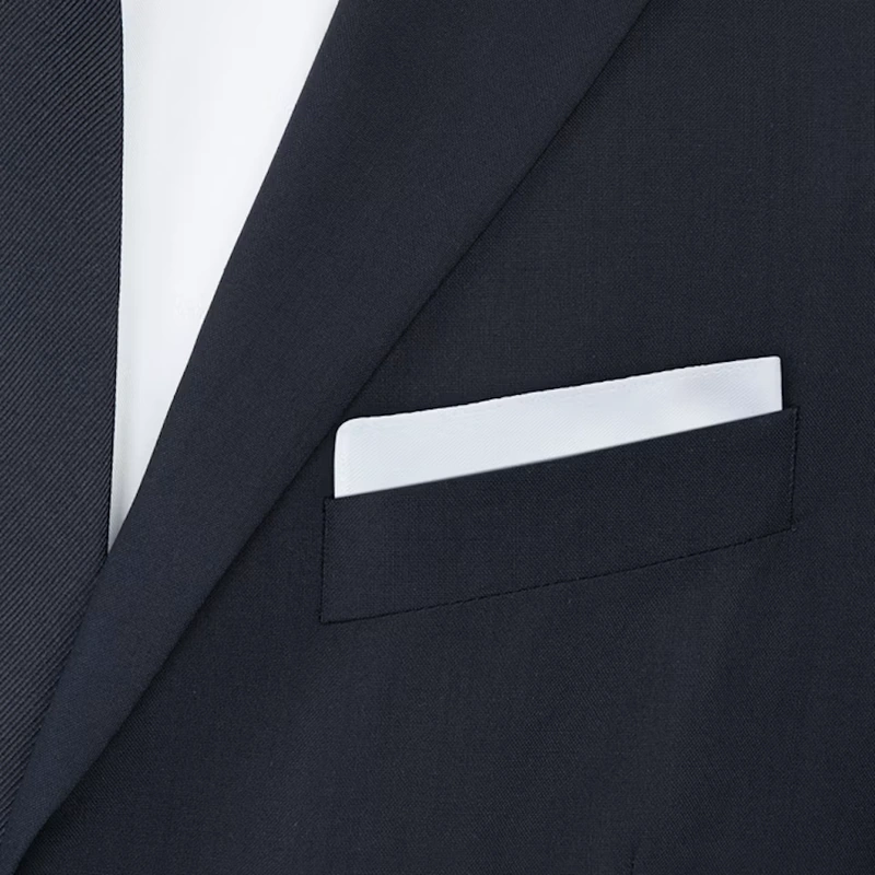 White pocket square in a flat fold in the breast pocket of a navy jacket