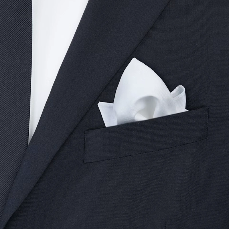 White pocket square folded as a puff in the breast pocket of a navy jacket