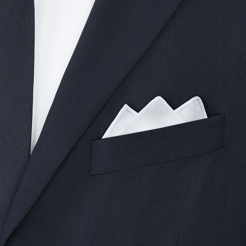 White pocket square with three points up in the breast pocket of a navy jacket